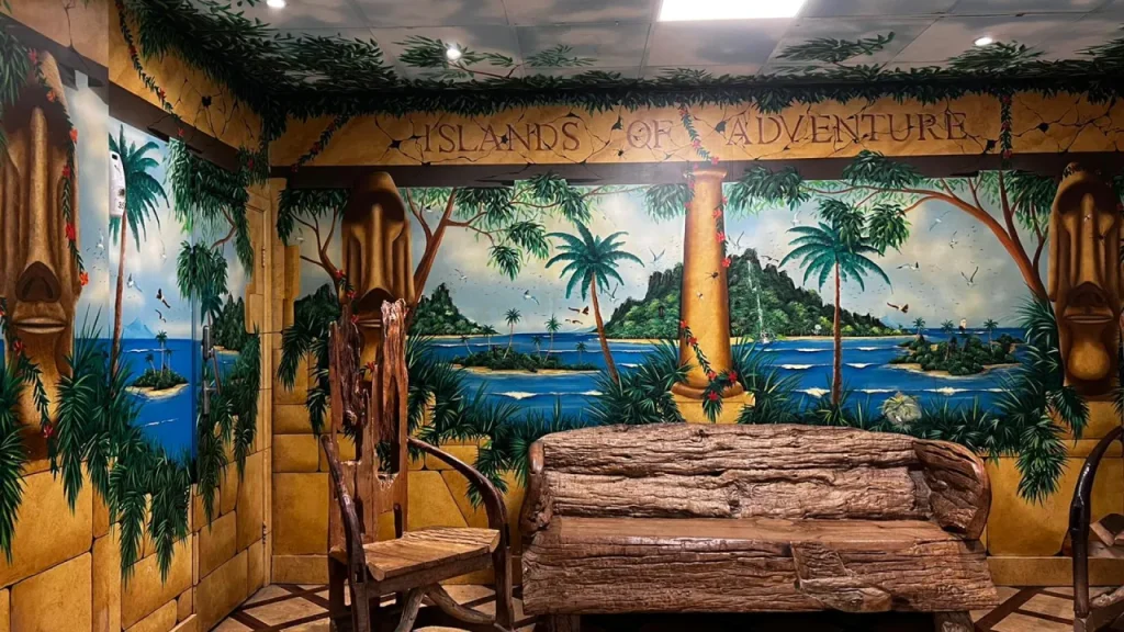 Themed seating area inside Sandcastle Waterpark in Blackpool with an ‘Islands of Adventure’ tropical wall mural, carved-style bench, and wooden chair.