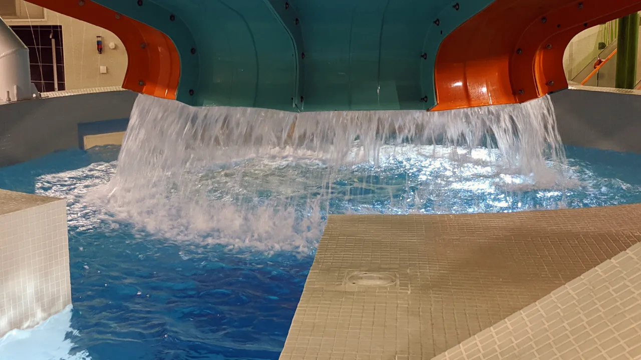 Wide waterfall feature pouring from a large teal and orange structure into an indoor pool at The Wave Waterpark in Coventry.