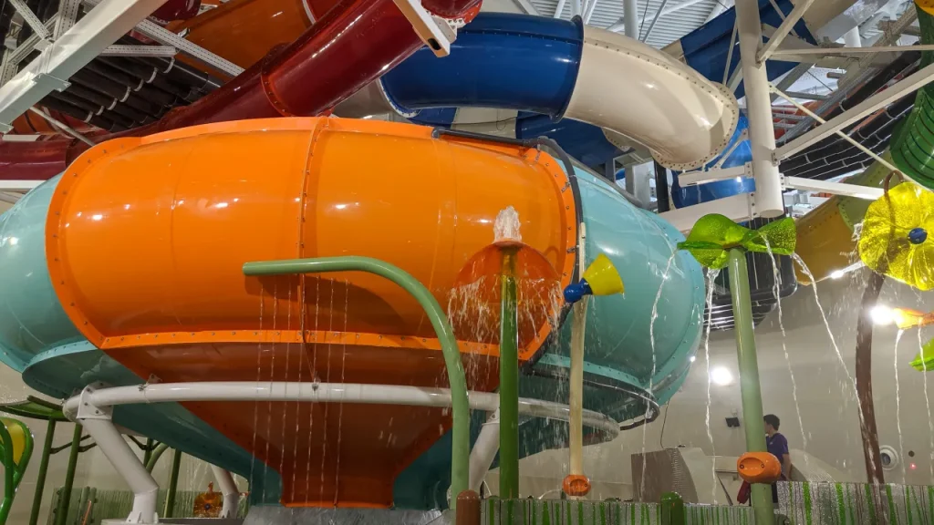 Close-up of large orange and teal enclosed tube slide sections and water sprays inside The Wave Waterpark in Coventry, with additional flumes overhead.