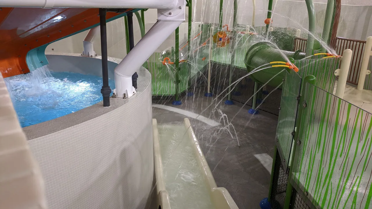 Children’s splash area at The Wave Waterpark in Coventry with water jets and spray features, a small slide channel, and enclosed play sections beside the main slide structure.
