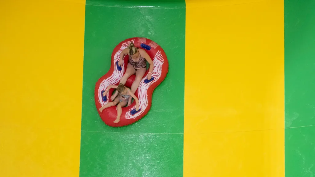 Overhead view of an adult and child riding a red inflatable raft down a green water slide lane at The Wave Waterpark in Coventry.