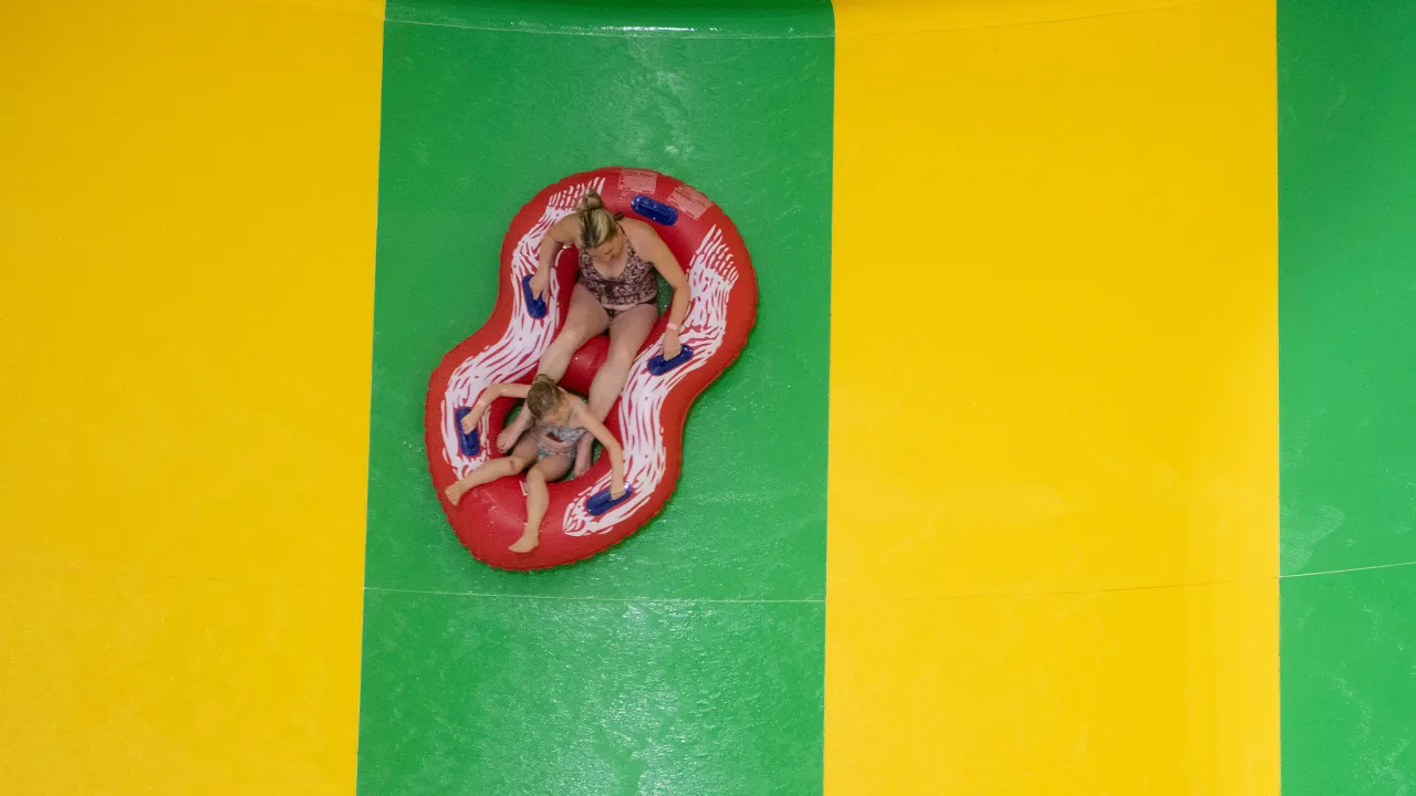 Overhead view of an adult and child riding a red inflatable raft down a green water slide lane at The Wave Waterpark in Coventry.