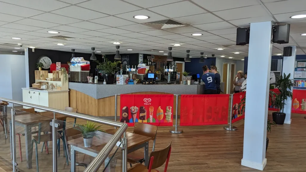 Indoor café and reception counter at Aqua Action, Fairlop Waters, with seating, drinks tills, and visitors ordering refreshments before heading to the lake activities.