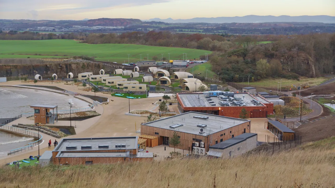 Panoramic view of Lost Shore Surf Resort in Scotland, showing the surf lagoon, resort buildings, and pod-style accommodation in a quarry setting.
