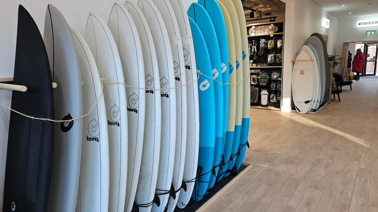 Row of surfboards in the Lost Shore Surf Resort surf shop and hire area in Scotland, showing multiple board sizes ready for lessons and surf lagoon sessions.