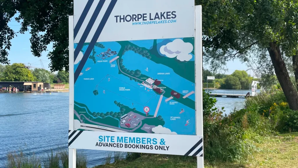 Thorpe Lakes signboard showing a site map with labelled areas including the Aqua Park, cable wake park, reception, and surrounding lakes beside the water.